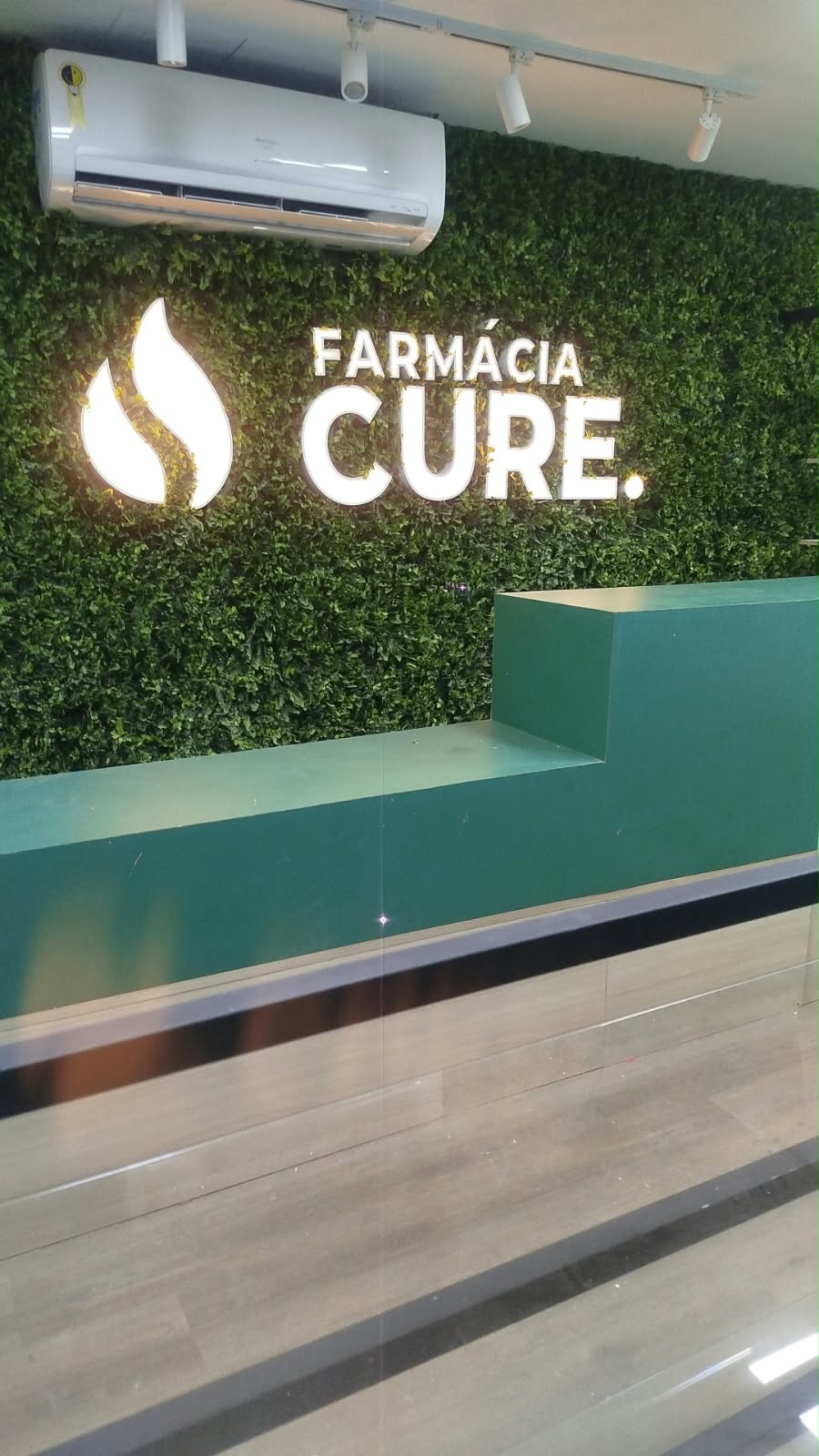 Recepção da Farmácia CURE na Savassi, com balcão verde e letreiro iluminado